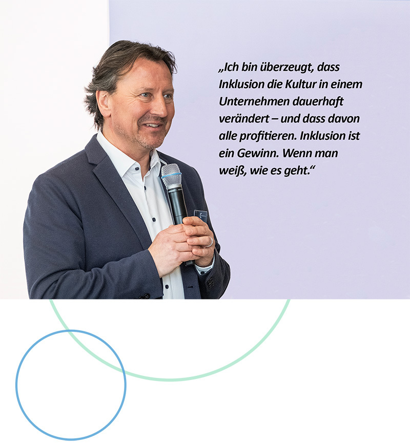 Olaf Guttzeit ist leicht von der Seite zu sehen, er trägt einen blauen Blazer, ein weißes Hemd und spricht in ein Mikrofon.  Daneben steht als Zitat: „Ich bin überzeugt, dass Inklusion die Kultur in einem Unternehmen dauerhaft verändert – und dass davon alle profitieren. Inklusion ist ein gewinn. Wenn man weiß, wie es geht.“
