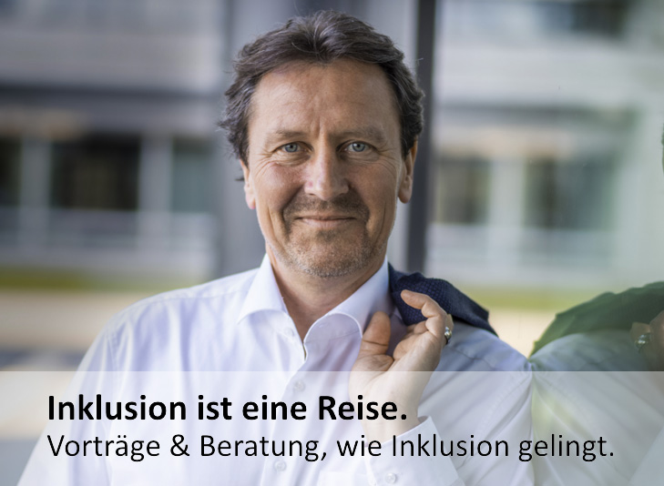 Olaf Guttzeit ist leicht von der Seite zu sehen, er trägt einen blauen Blazer, ein weißes Hemd und spricht in ein Mikrofon.